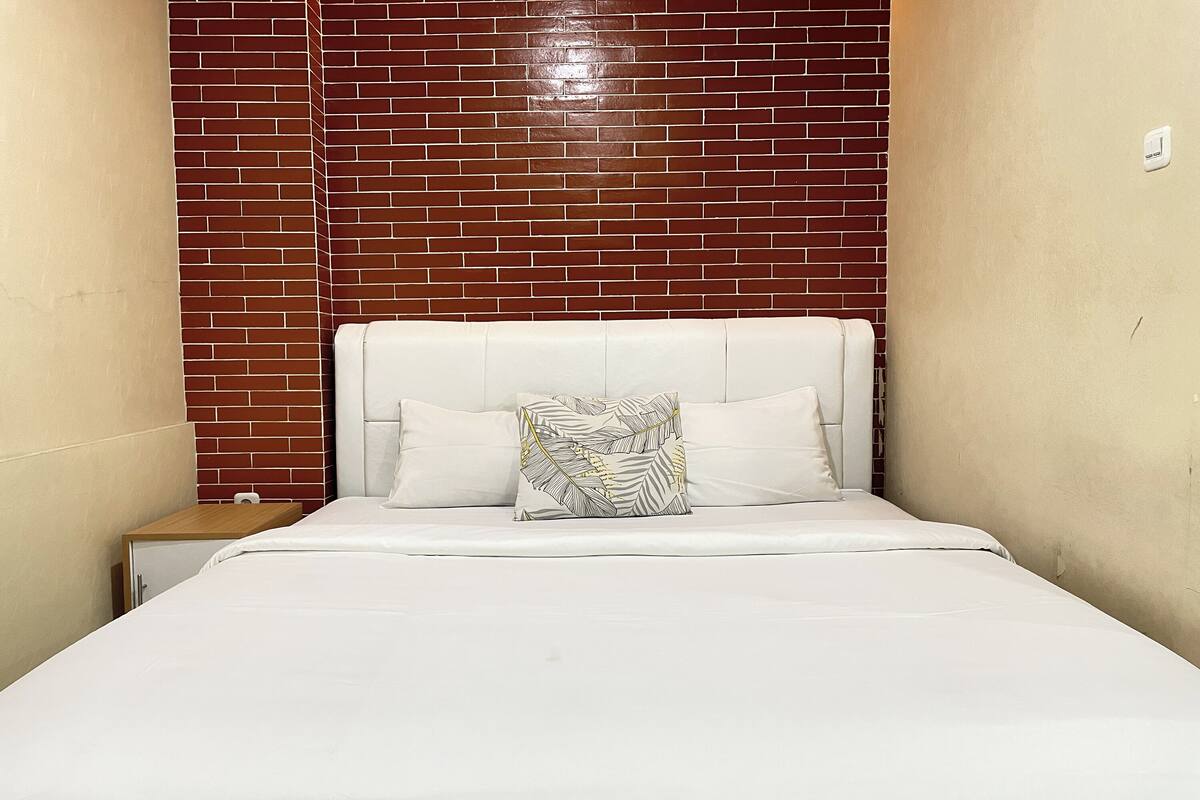 A bed with white bedding and a leaf-patterned pillow, set against a brick wall.