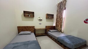 A small, compact room with two single beds, a wooden desk, a mirror, and a window with curtains. - Jirek Homestay Bukittinggi (Bukittinggi)