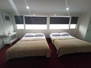 Una habitación con dos camas, una mesita y un ventanal.