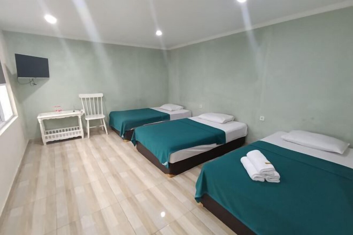 Habitación de hotel con tres camas, una mesita y un televisor montado en la pared.