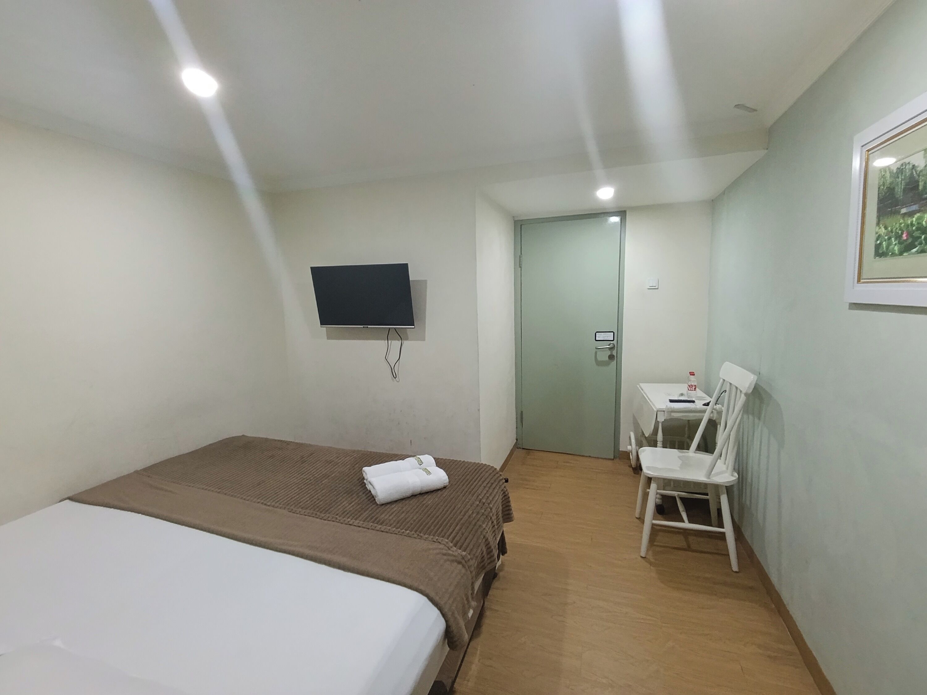 Habitación de hotel con cama, televisor montado en la pared, escritorio con silla y puerta que da a otra habitación.