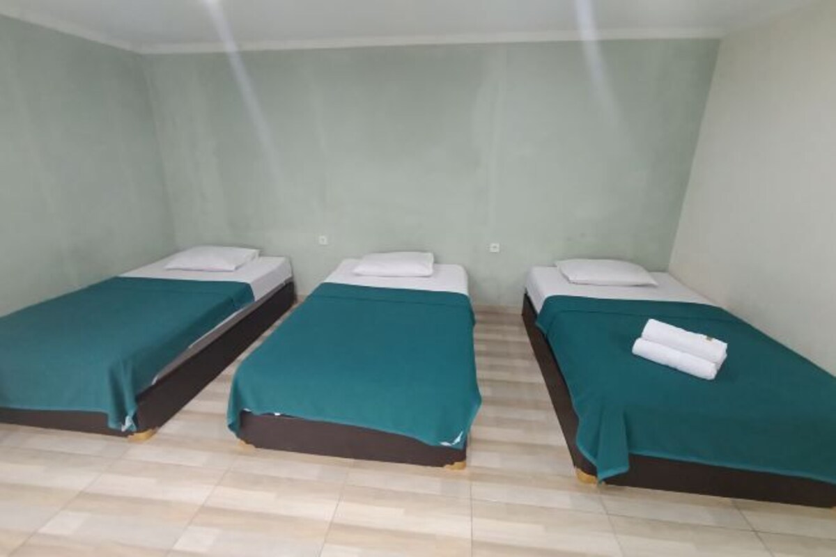 A room with three single beds, each with a teal bedspread and white pillows.