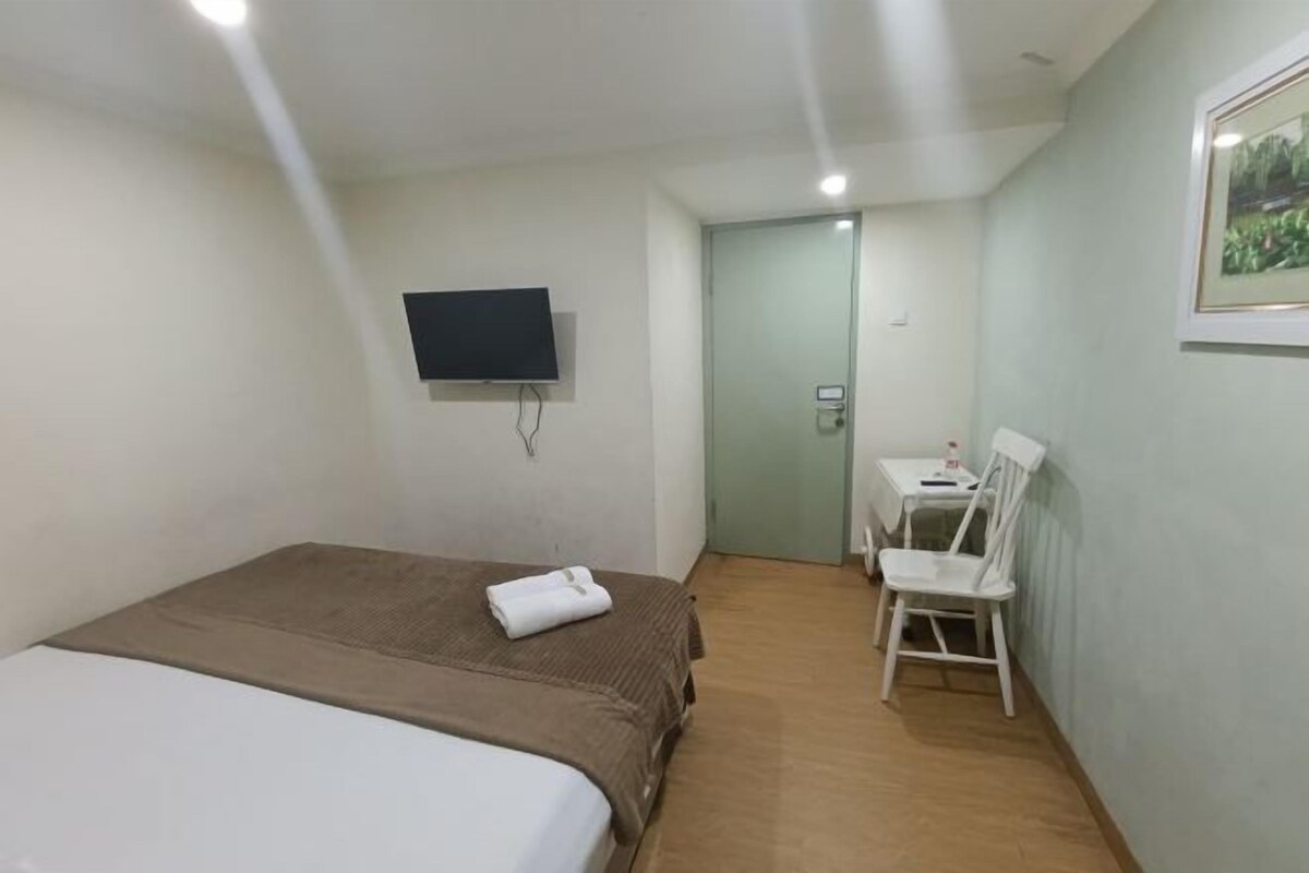 A hotel room with a bed, a desk, a chair, a television, and a door.