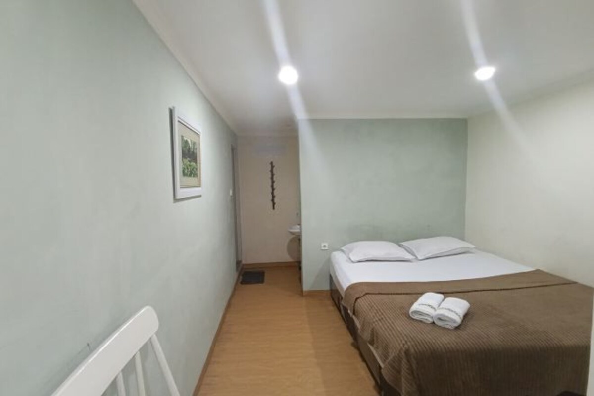 A small, clean room with a single bed, a framed picture on the wall, and a light fixture above the bed.