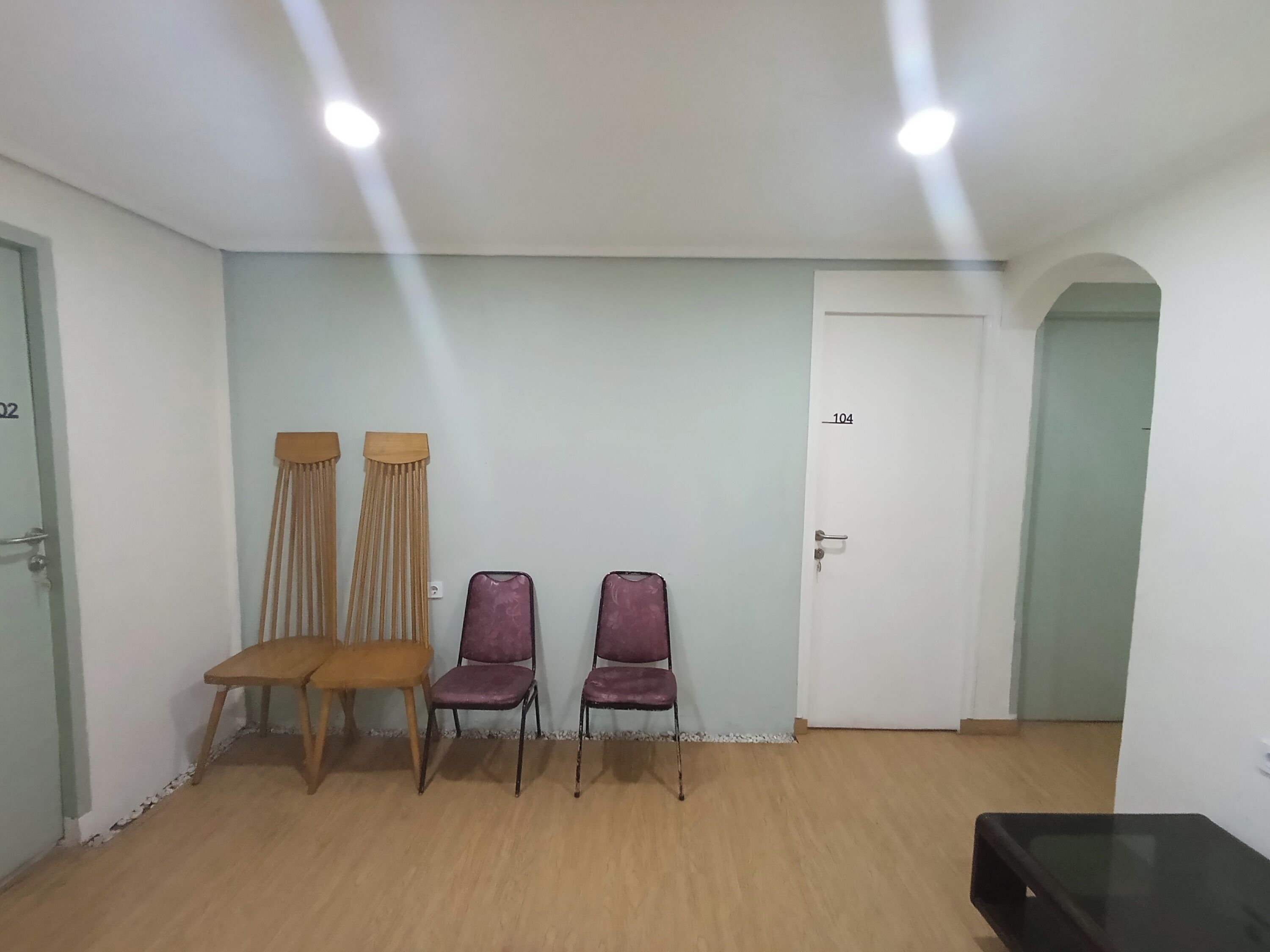 Een kamer met twee houten stoelen, twee paarse stoelen, een zwarte tafel en een witte deur met het nummer 104.