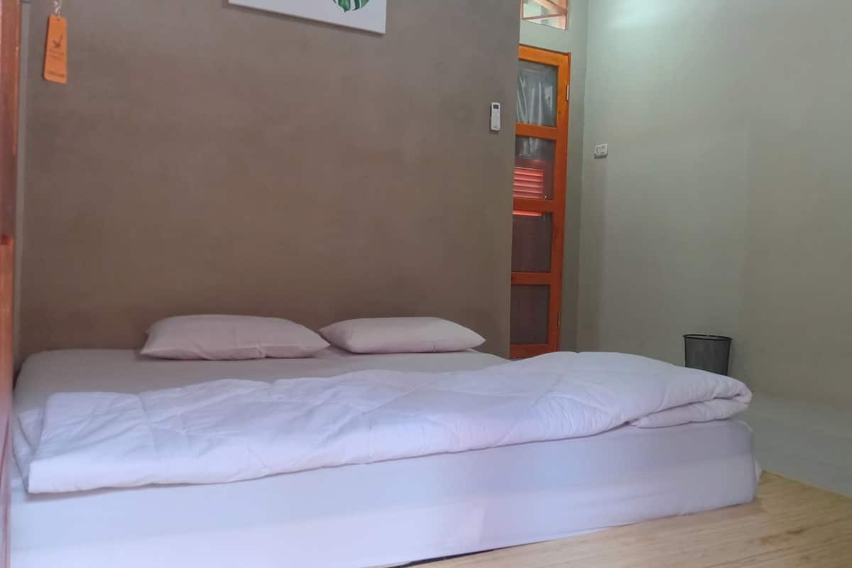 A single bed with a white duvet and two pillows, a wooden headboard, and a small bedside table with a lamp.