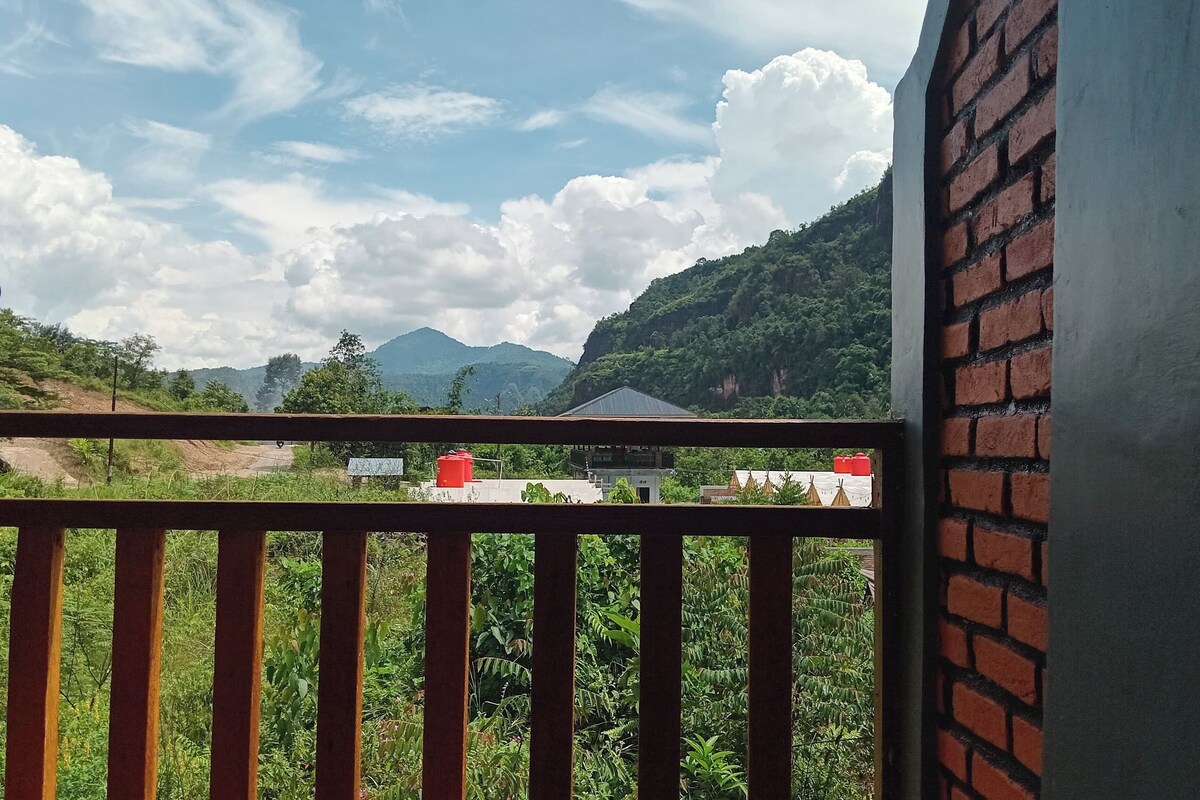 A balcony with a view of a mountainous landscape, a brick wall, and a building with a red roof.
