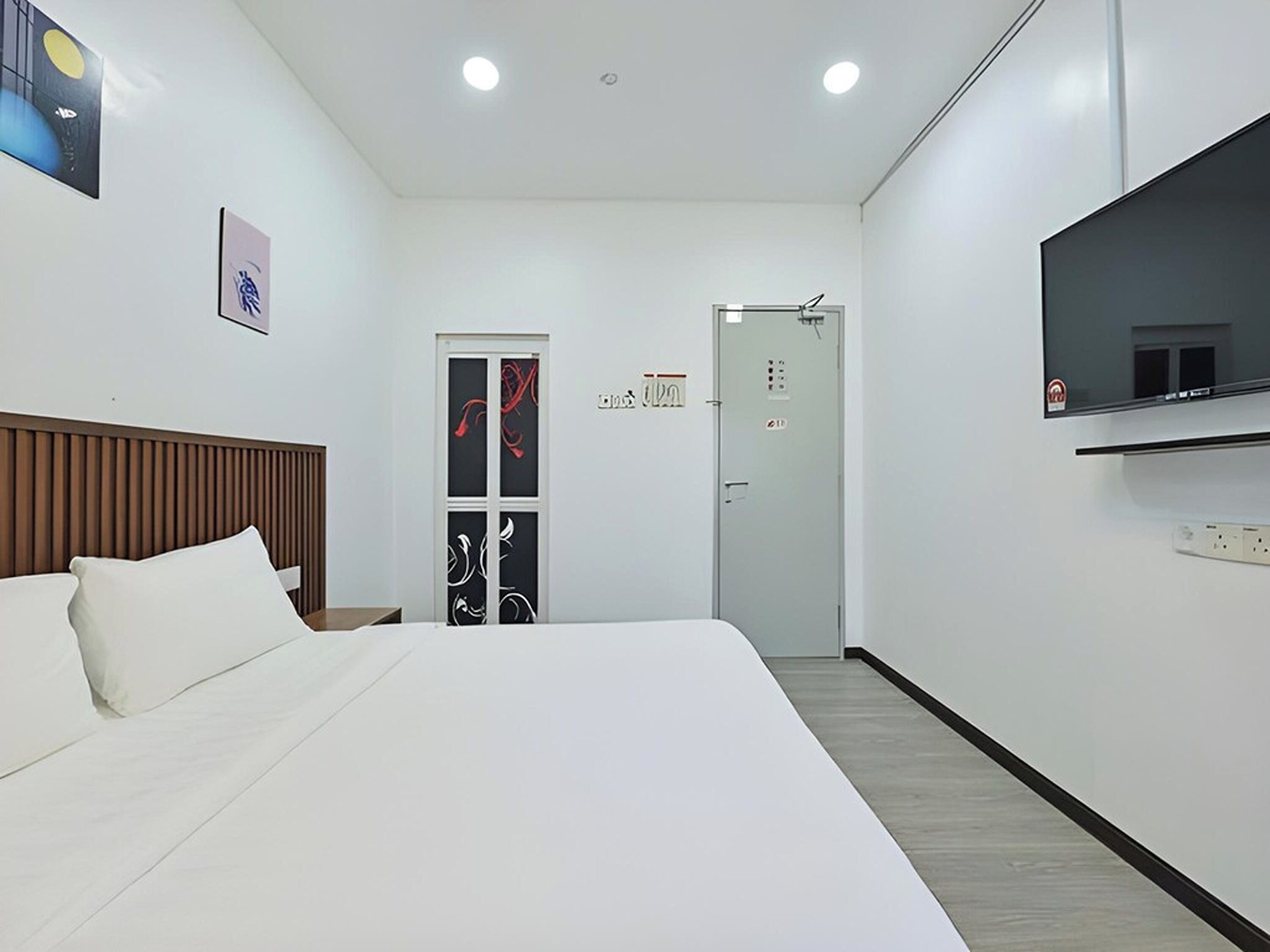 A modern hotel room with a large bed, a TV mounted on the wall, and a door leading to a bathroom.