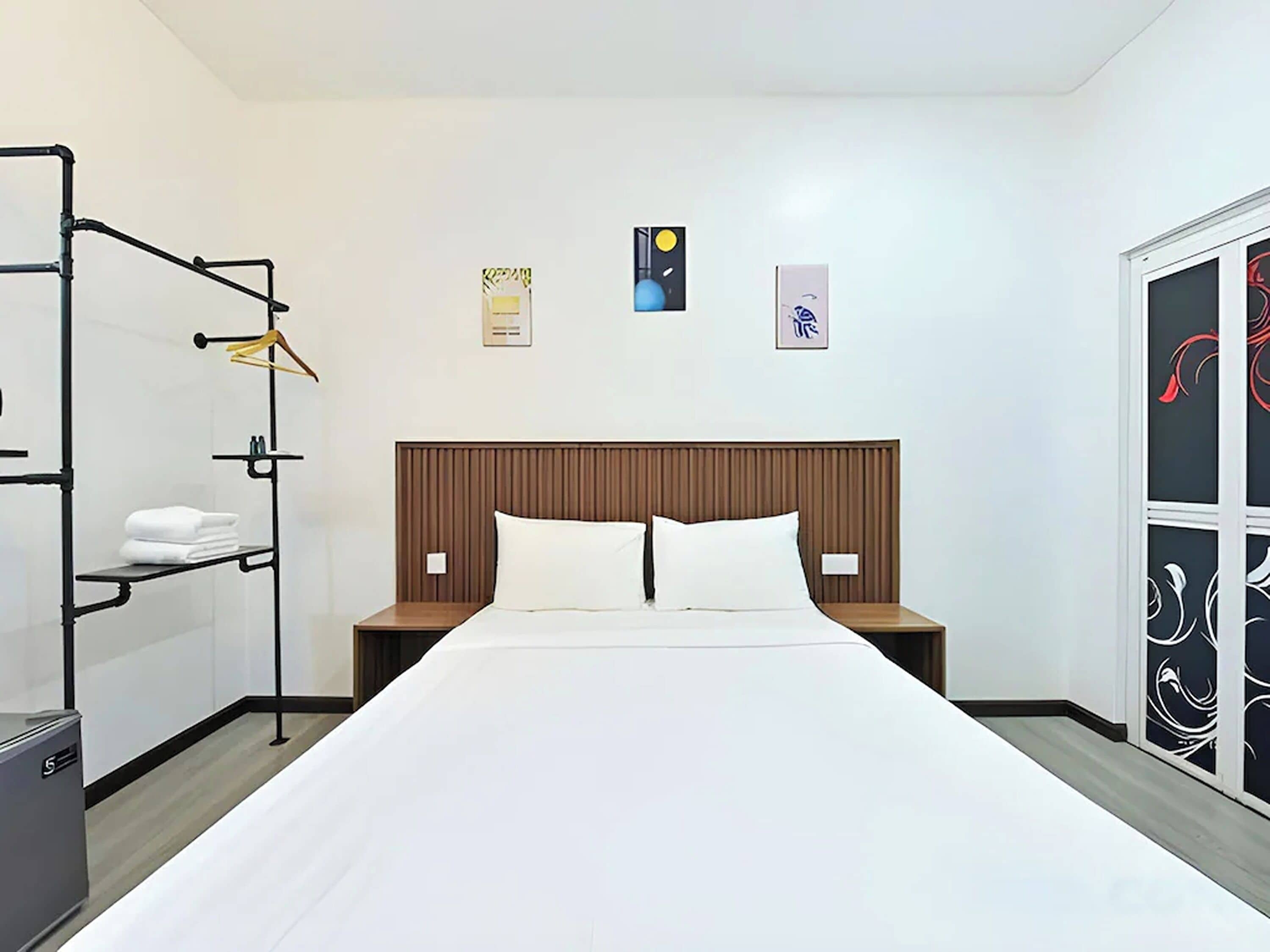 Una habitación de hotel con una cama, dos mesitas de noche, un armario y un estante con toallas.