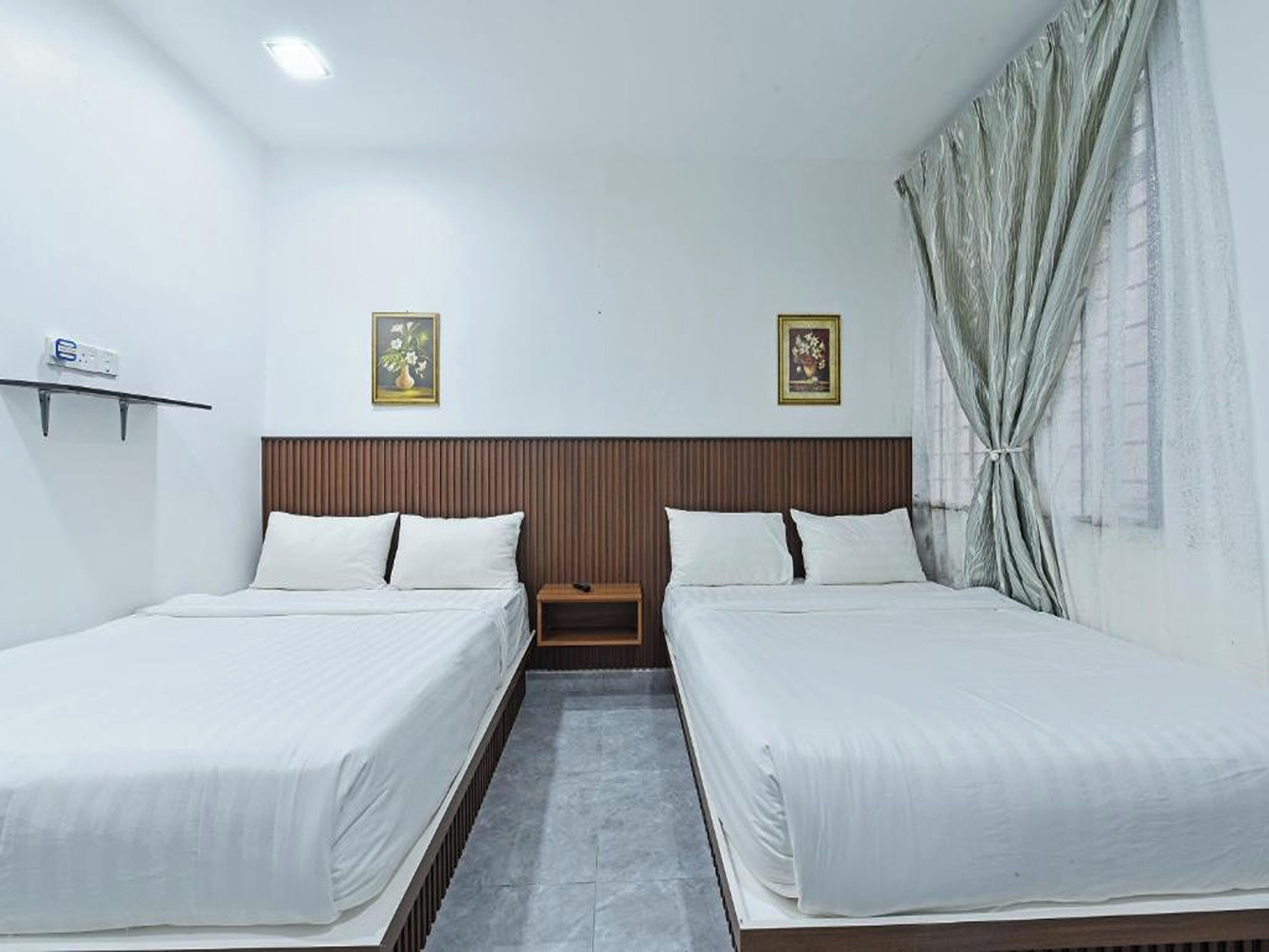 Habitación de hotel con dos camas individuales, un cabecero de madera, una mesita de noche y un estante fijado a la pared.