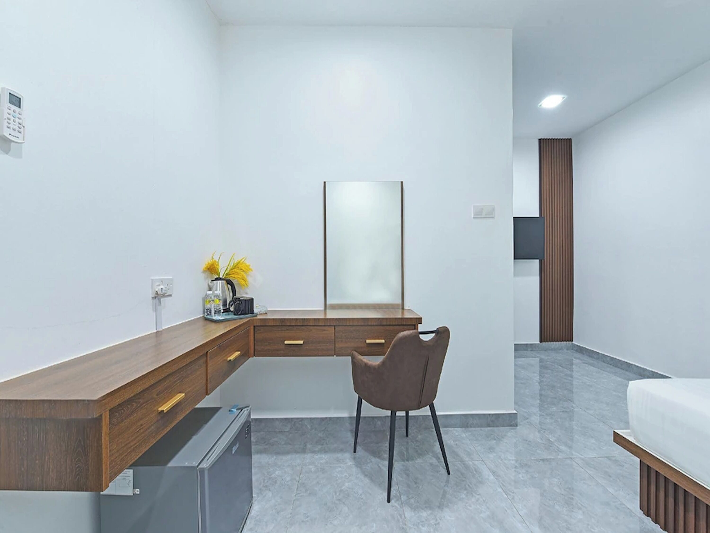 Una habitación de hotel moderna con un escritorio de madera, una silla, un refrigerador pequeño, un espejo y una cama.