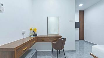 Una habitación de hotel moderna con un escritorio de madera, una silla, un refrigerador pequeño, un espejo y una cama.