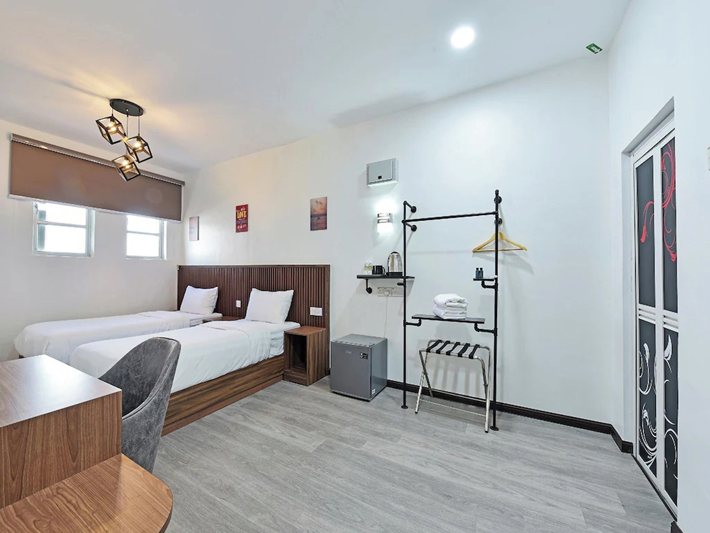 A hotel room with two single beds, a desk, a chair, a wardrobe, and a drying rack.