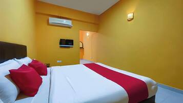 A hotel room with a bed, pillows, a TV, and an air conditioning unit.
