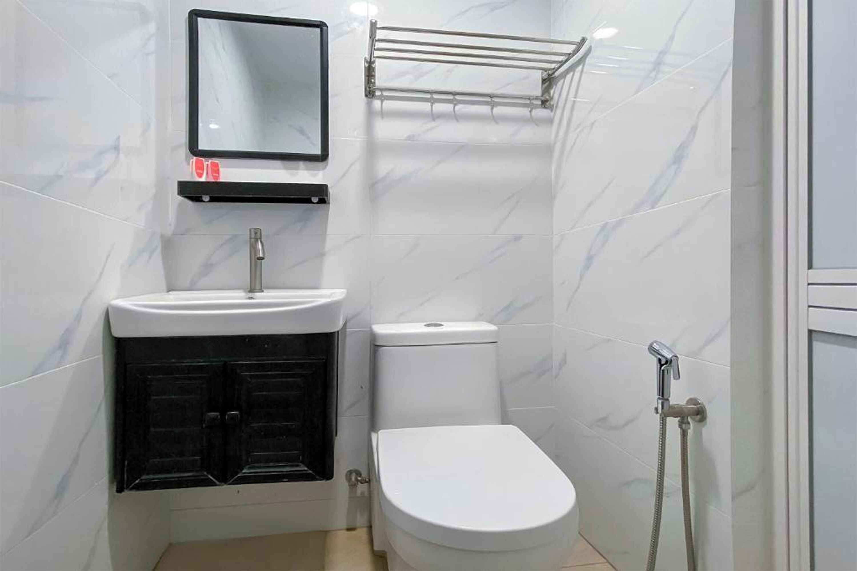 Une petite salle de bain avec des toilettes blanches, un meuble noir, un lavabo blanc, un miroir et un espace douche.