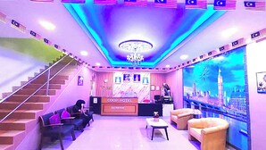 A hotel reception area with a staircase, reception desk, seating area, and a large window with a cityscape view. - Coop Hotel Kangar (Kangar)