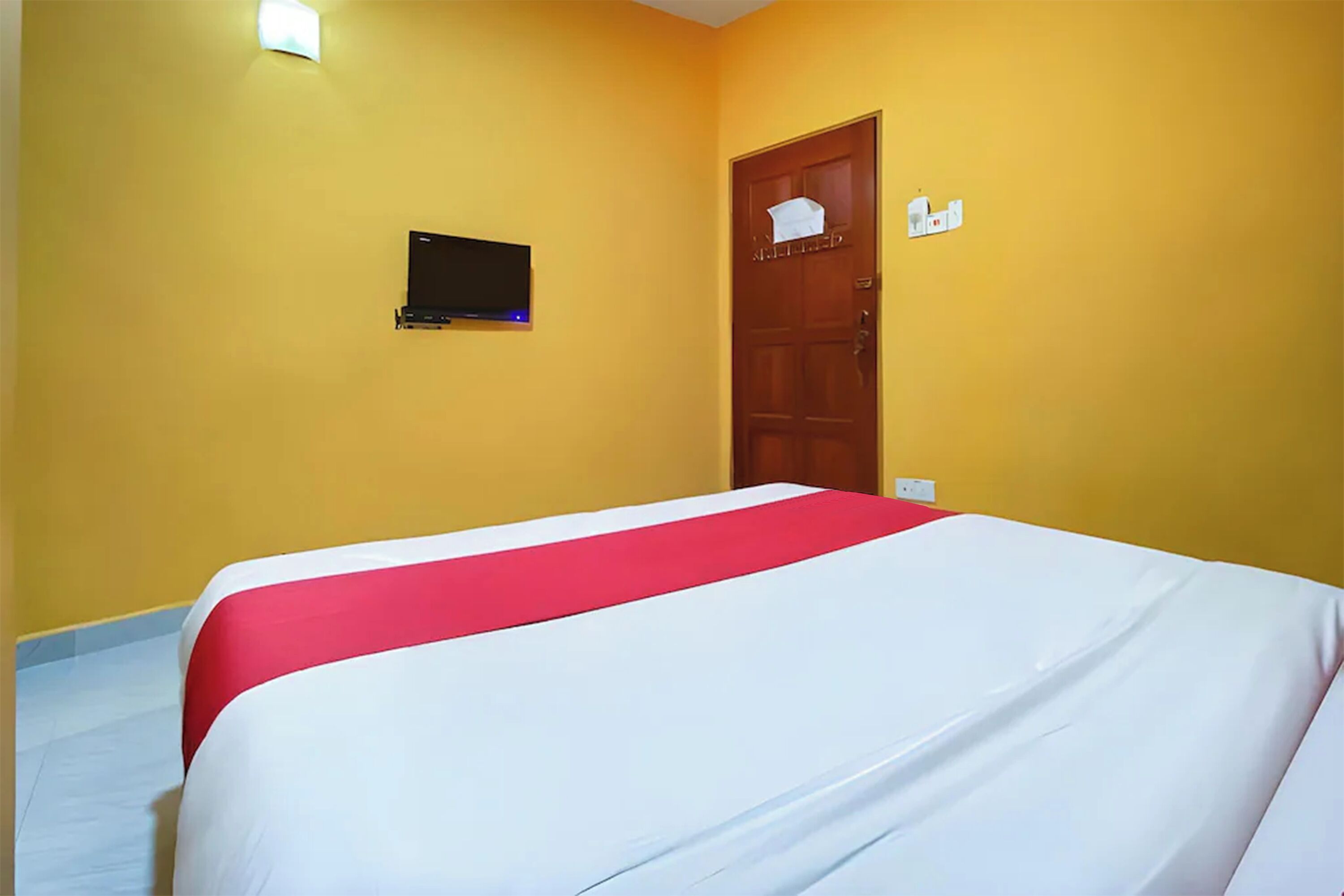 Habitación de hotel con cama, televisor montado en la pared y una puerta con un letrero.