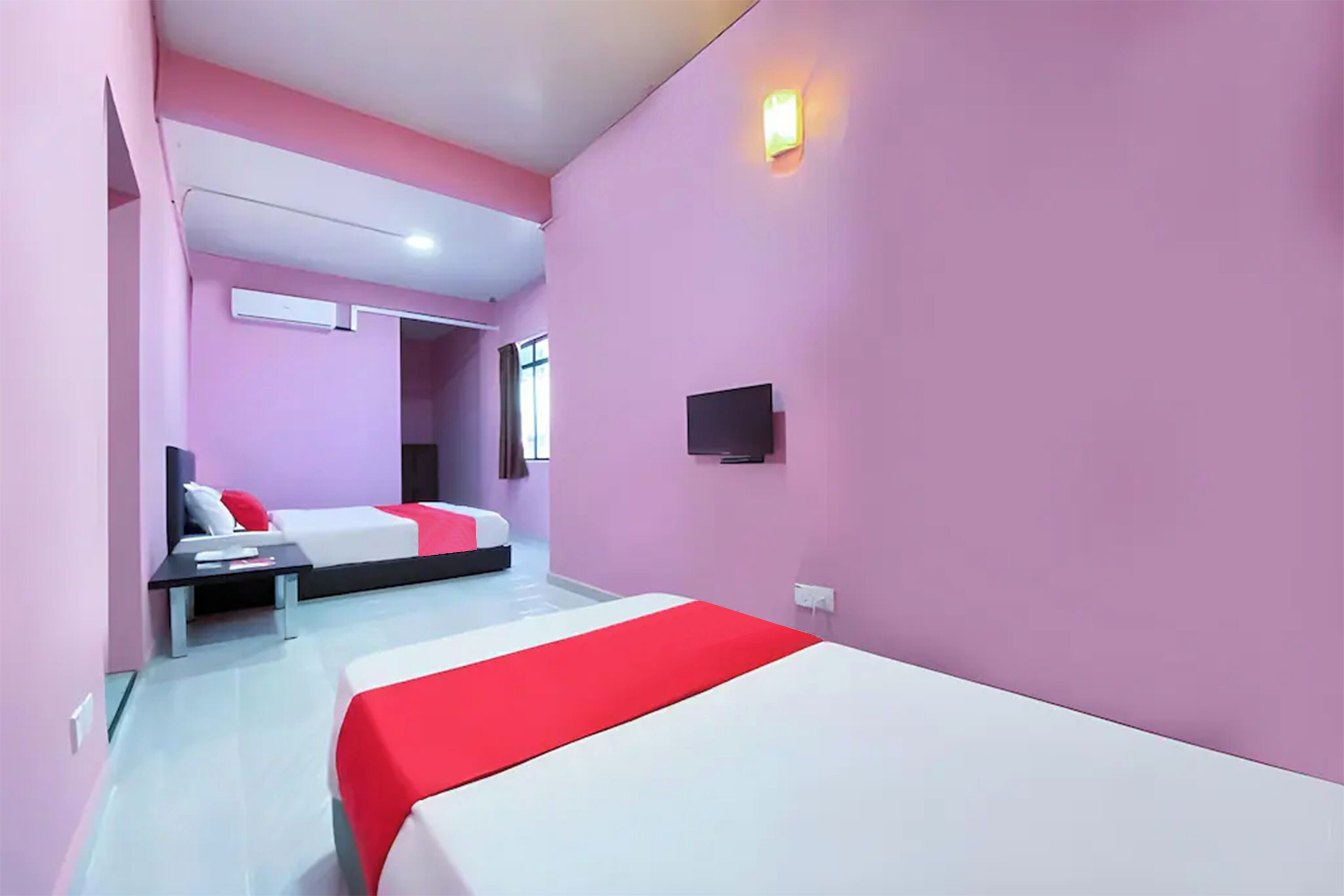 A hotel room with two beds, a flat-screen TV, a bedside table, and a window with curtains.
