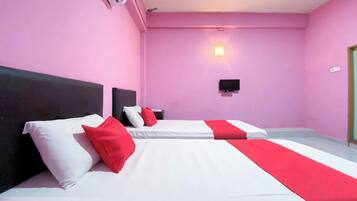 Habitación de hotel con dos camas, cada una con ropa de cama blanca y detalles rojos, paredes rosas, un televisor montado y una mesita de noche con una lámpara.