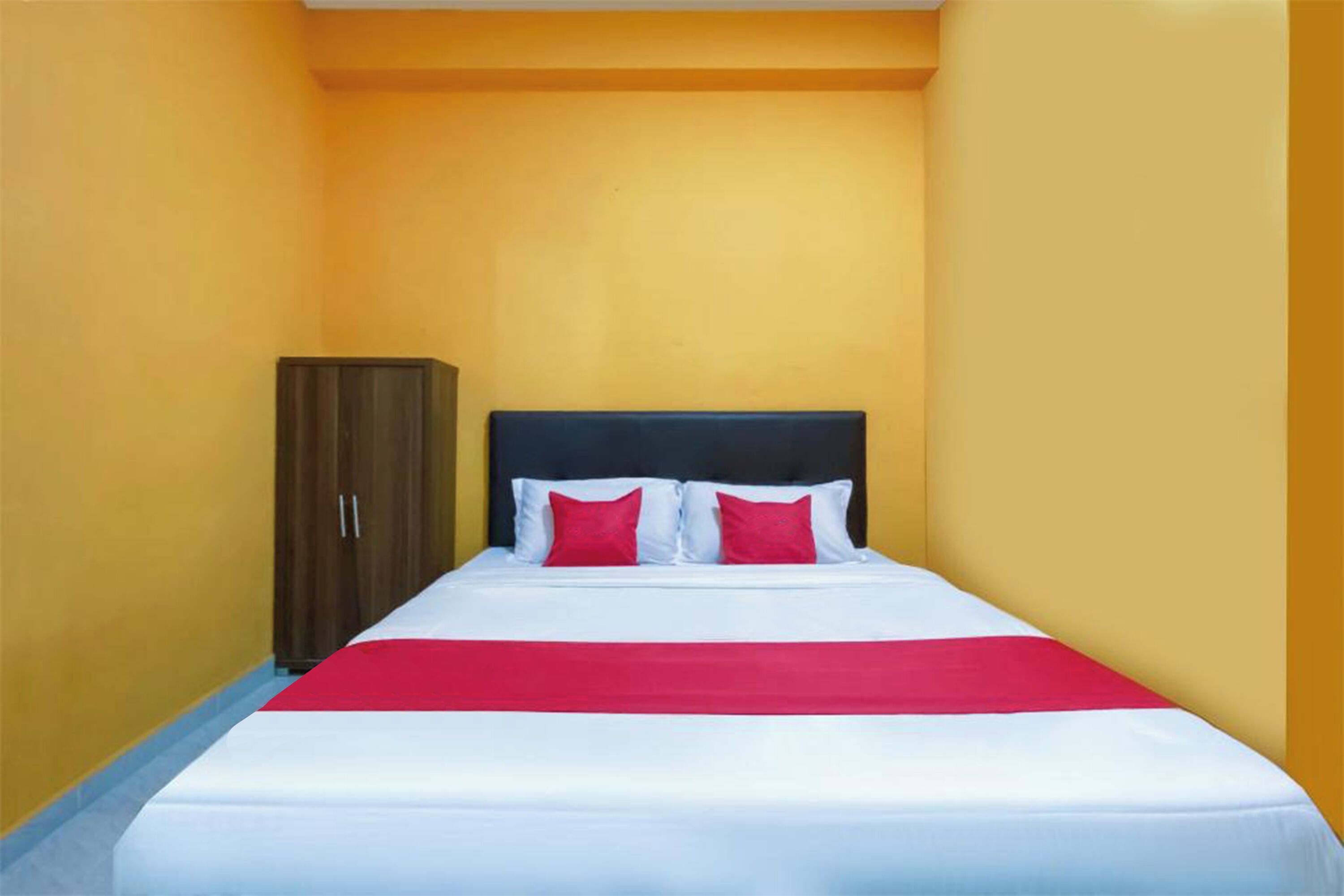 A hotel room with a bed, a wardrobe, and a red accent on the bedspread.