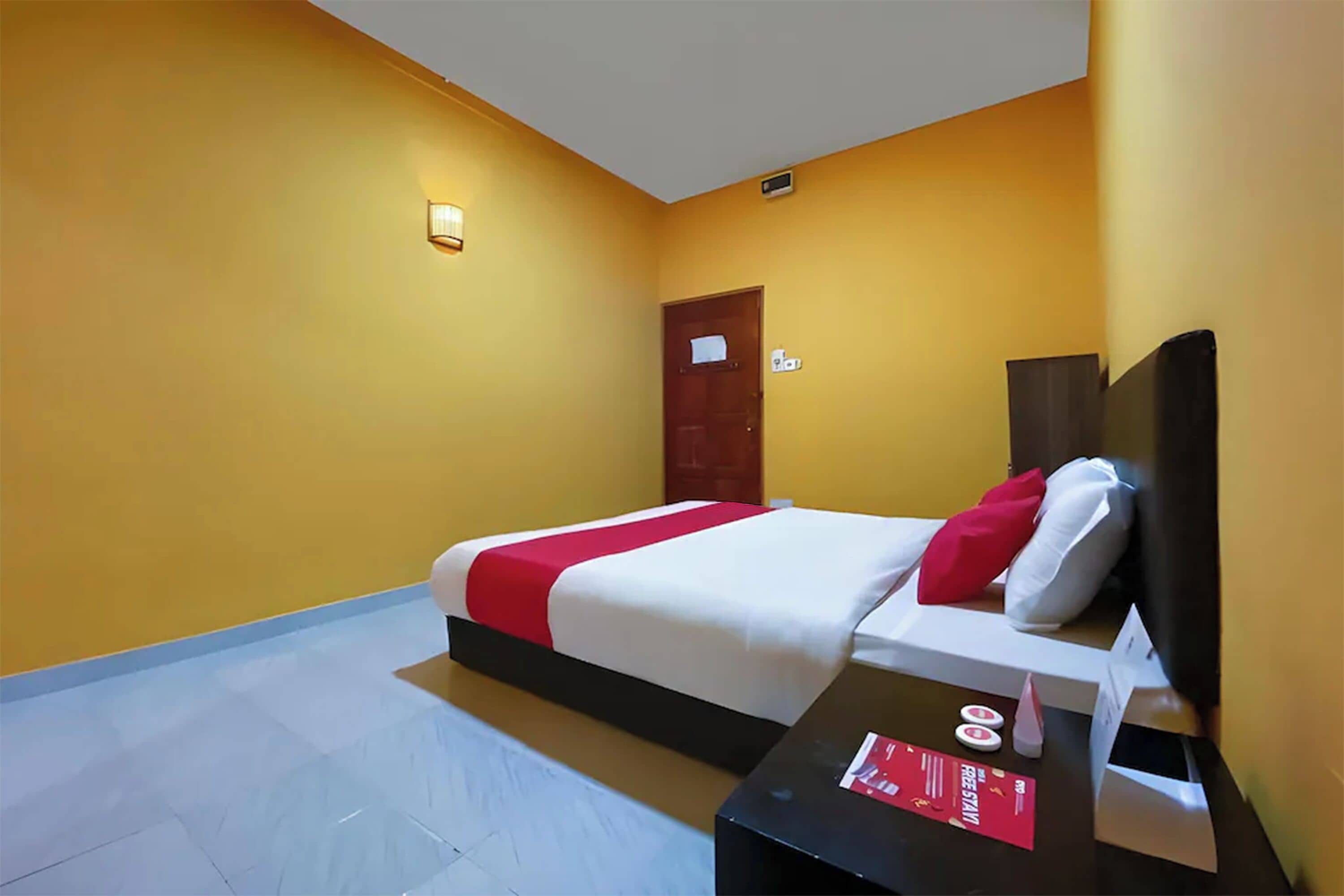 A hotel room with a bed, a nightstand, a wall-mounted light, and a door.