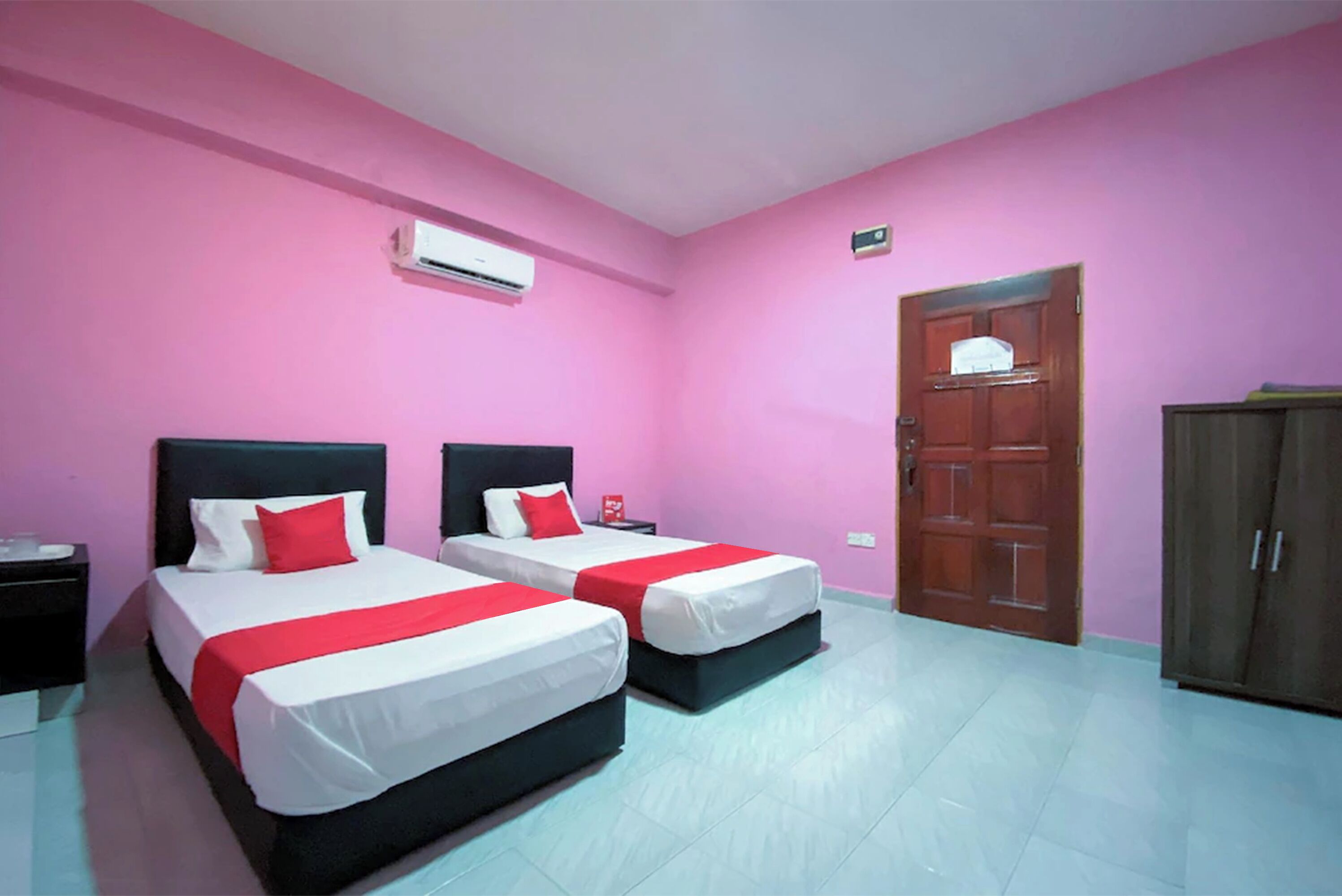 A room with two beds, pink walls, a wooden door, and a wardrobe.
