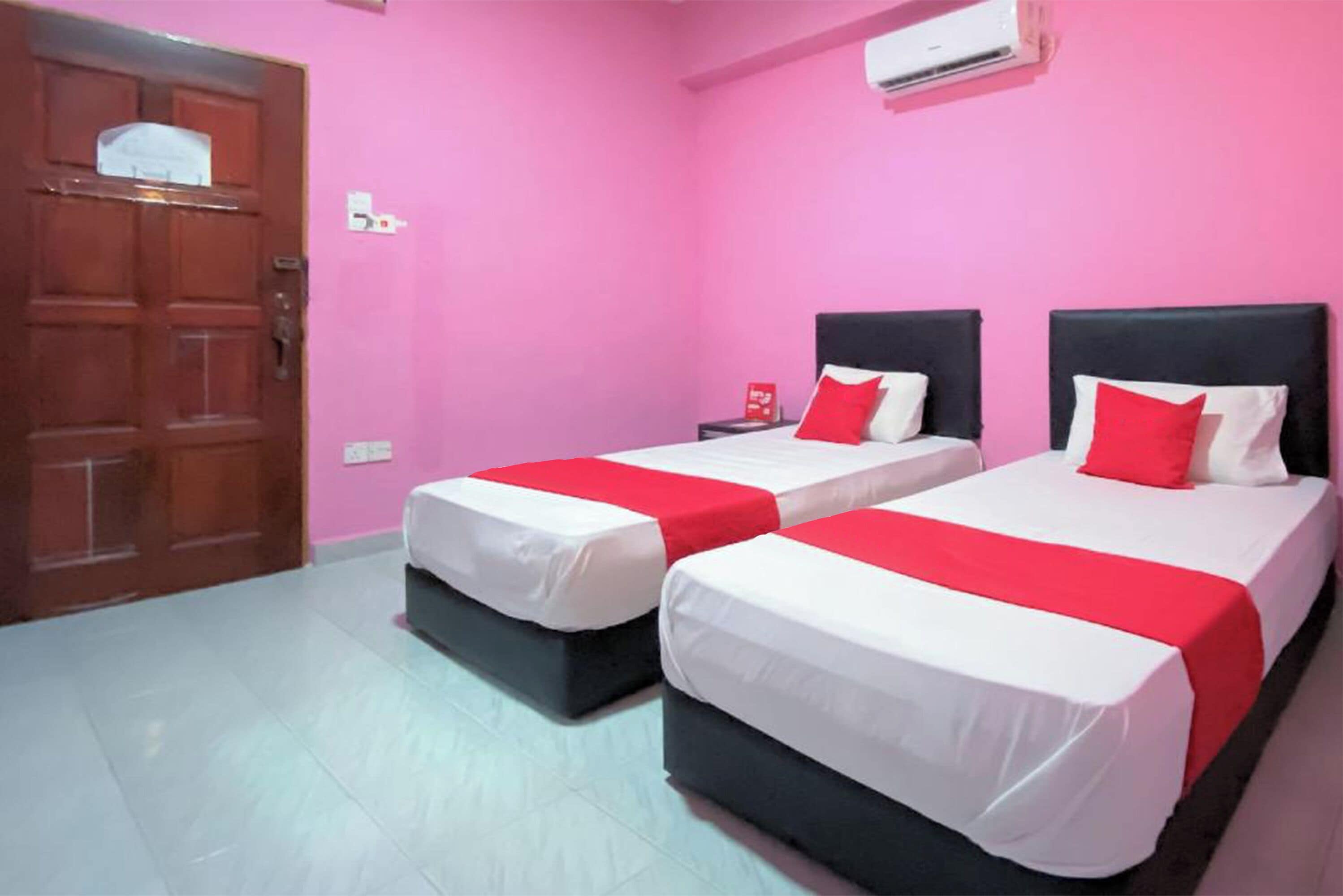 A room with two beds, pink walls, and a wooden door.