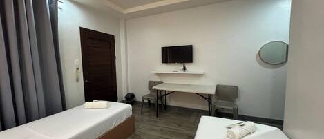 A hotel room with two single beds, a desk, a chair, a TV, and a small round mirror.