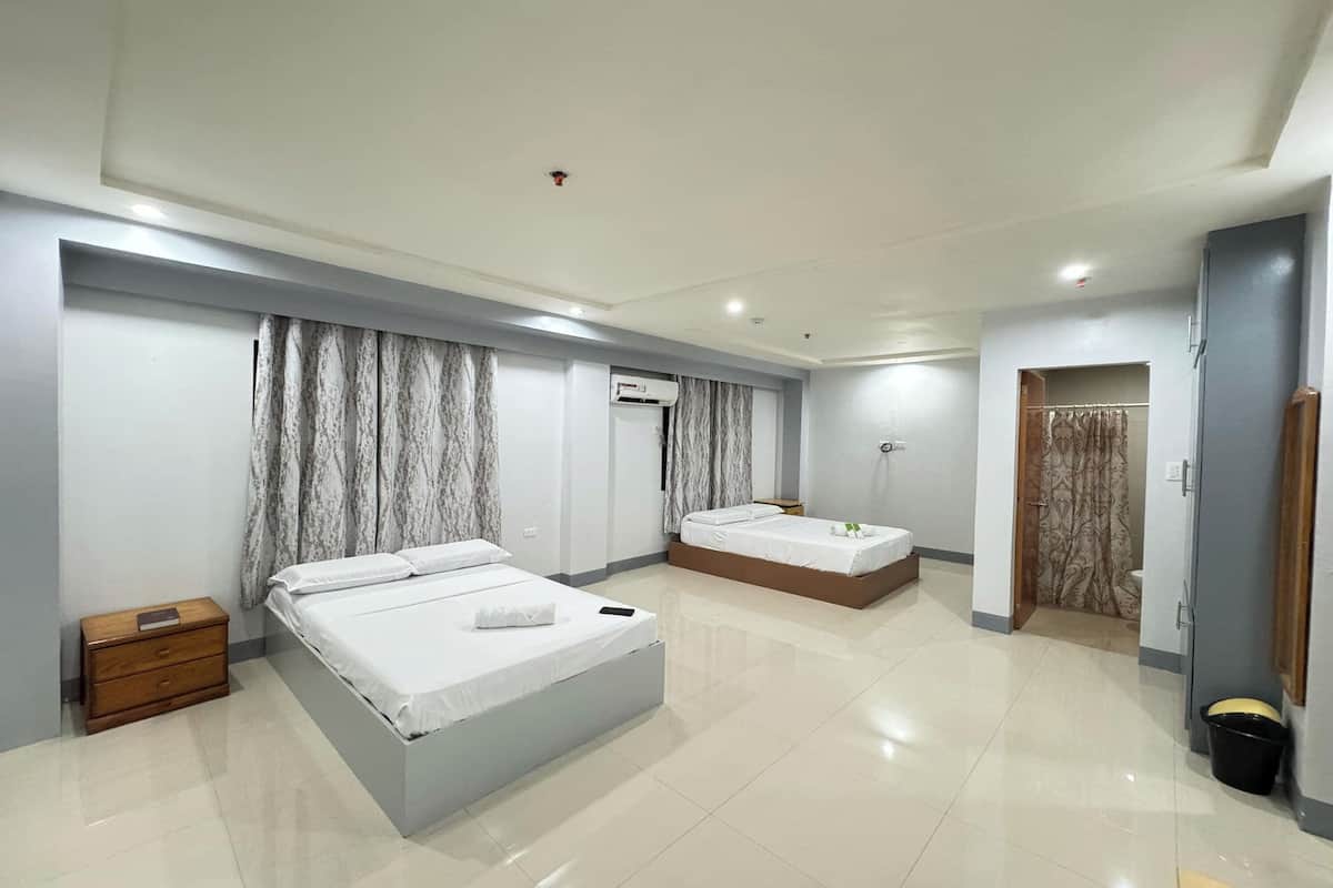Ein modernes Hotelzimmer mit zwei Betten, einem Holznachttisch, einer Klimaanlage und einem durch eine offene Tür einsehbaren Badezimmer.