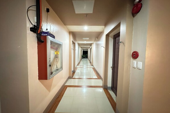 A long, narrow hotel corridor with a tiled floor, a fire alarm on the right, and a door at the end. - Hotel Ramon Bukidnon (Valencia)