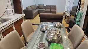 A dining area with a table set for four, a sofa, and a kitchenette in the background. - Tres Marias Farmhouse with Pool (Cuyapo)