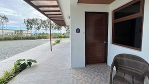 A covered outdoor area with a tiled floor, a wooden door, and a wicker chair.