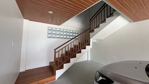 A modern interior with a wooden staircase, a car, and a wall with a geometric pattern.