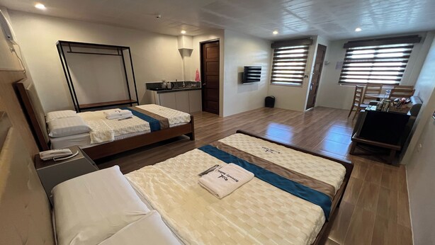 A hotel room with two beds, a small kitchenette, a TV, and a bathroom.