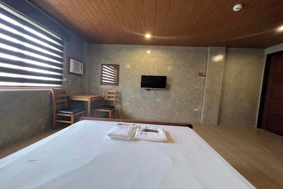 A hotel room with a large bed, a TV mounted on the wall, and a desk with a chair.