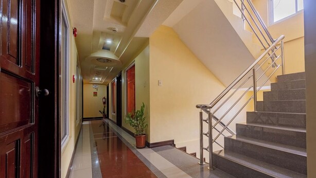 Un couloir d’hôtel avec un sol ciré, un escalier doté de rampes en métal et une plante en pot.