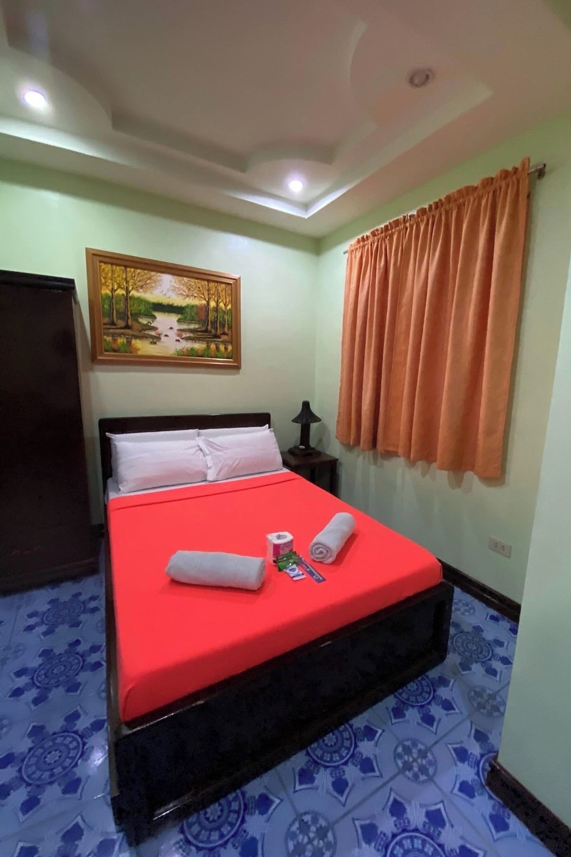 A room with a bed, a painting, a curtain, and patterned floor tiles.