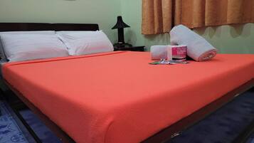 Una cama bien hecha con una colcha roja, almohadas blancas y una toalla enrollada al lado.