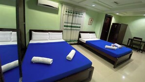 Une chambre d’hôtel avec trois lits simples, chacun doté d’un protège-matelas bleu et d’oreillers blancs. Un appareil de climatisation est fixé au mur, au-dessus des lits.