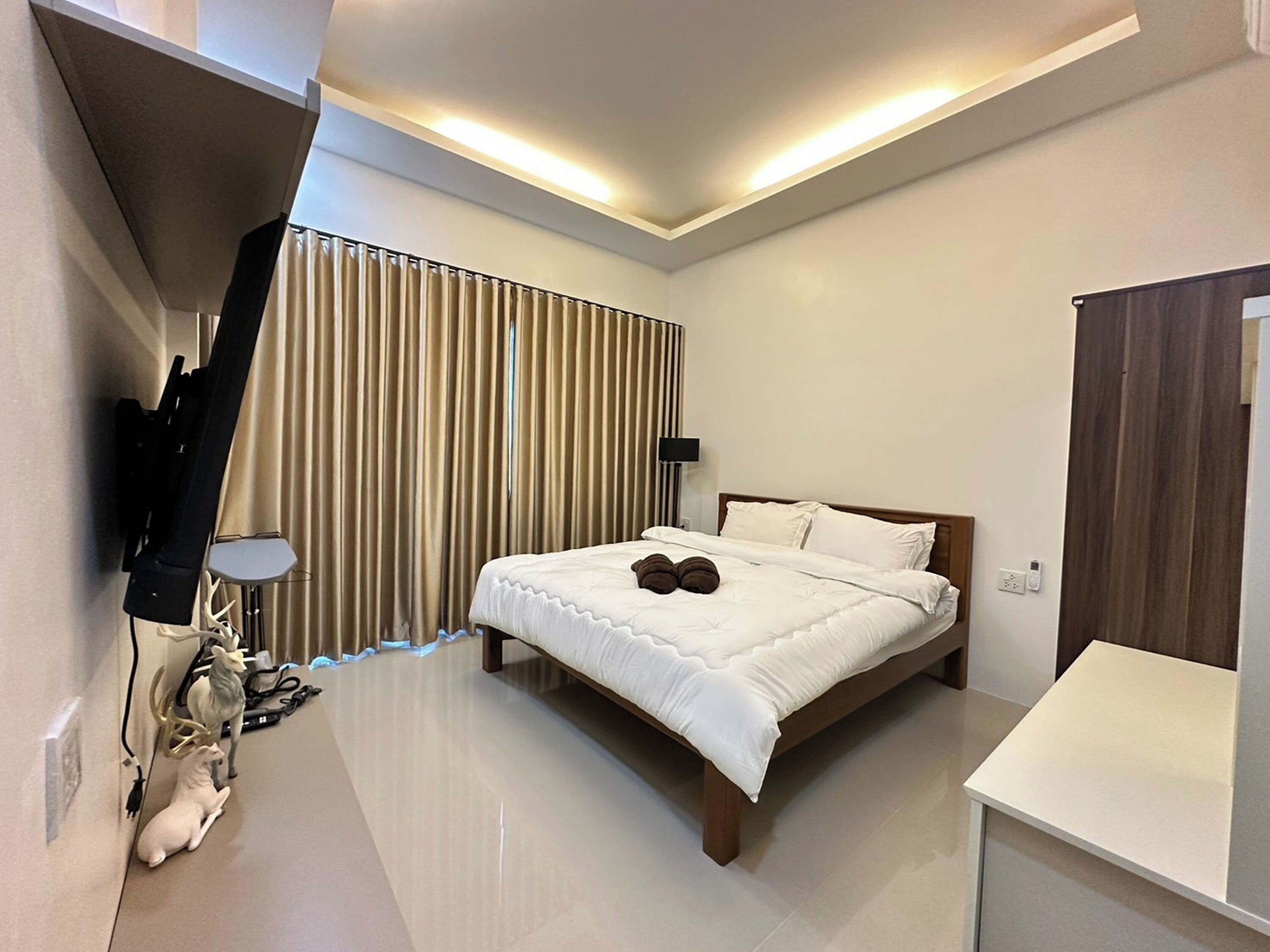 Une chambre d’hôtel moderne avec un grand lit, une table de chevet, un téléviseur fixé au mur et un rideau avec des stores verticaux.