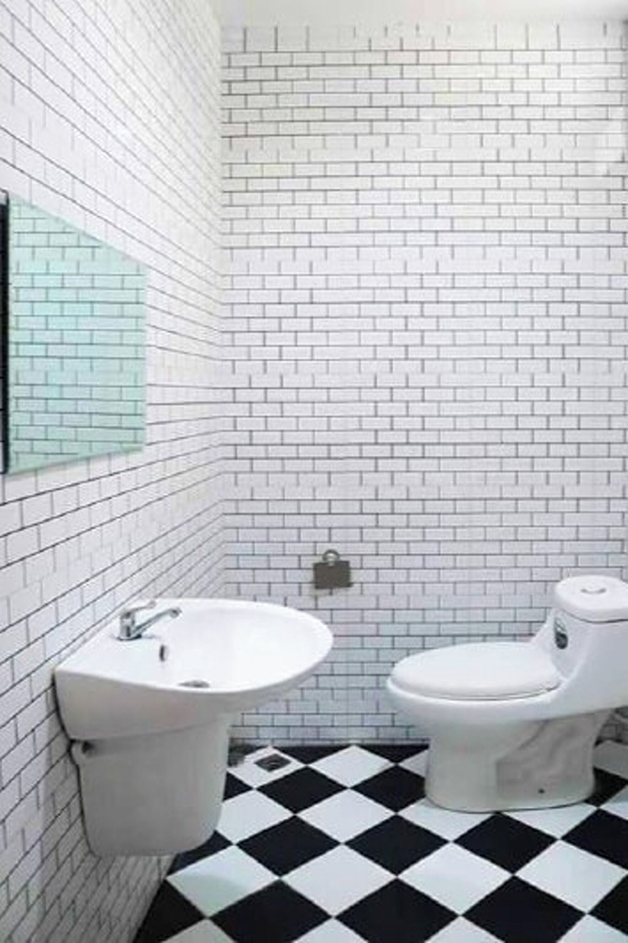 A bathroom with white subway tiles, a black and white checkered floor, a white sink, and a toilet.