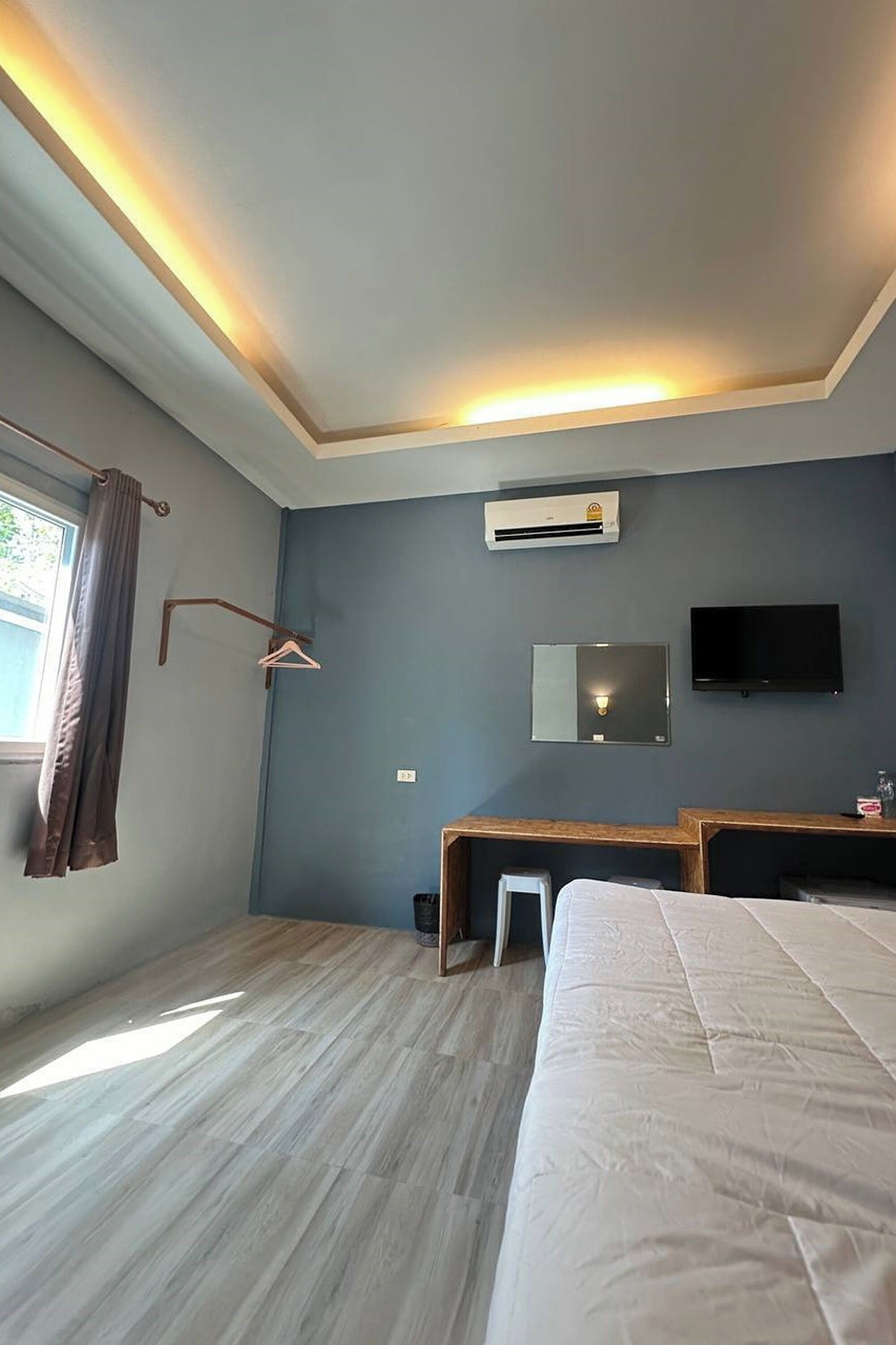 A bedroom with a bed, a desk, a chair, a TV, and an air conditioning unit.