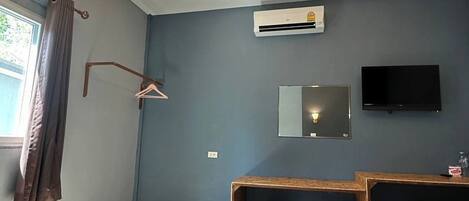 A bedroom with a bed, a desk, a chair, a TV, and an air conditioning unit.