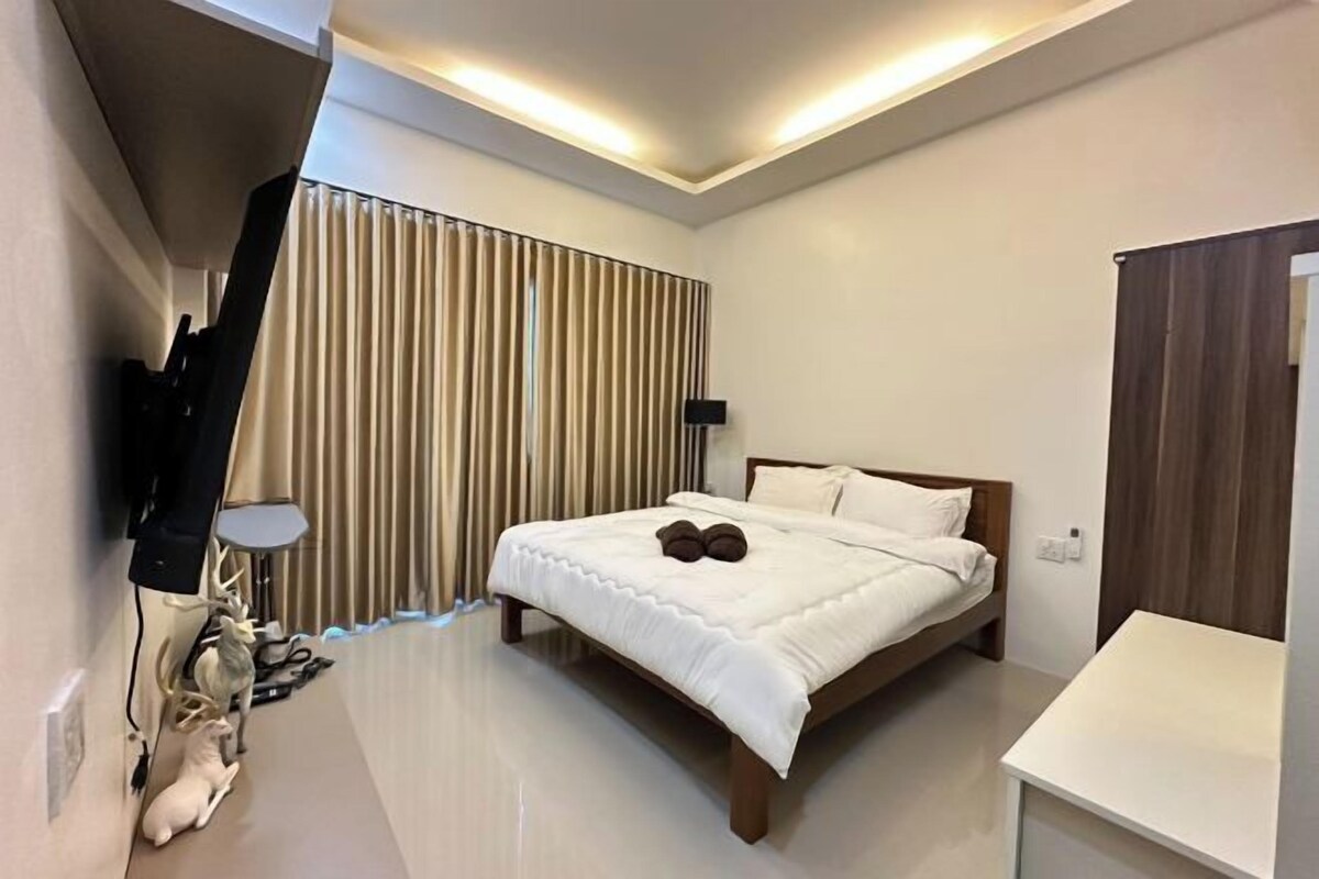 A modern hotel room with a bed, a TV, a desk, and a lamp.