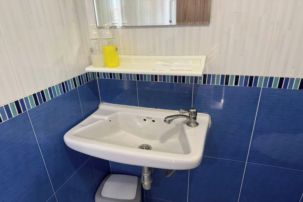 A bathroom with a white sink, blue tiles, a mirror, and a soap dispenser.