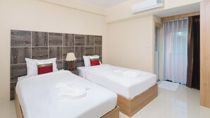 A hotel room with two beds, a wooden headboard, a window with curtains, and an air conditioning unit. - Good View Residence (Lampang)
