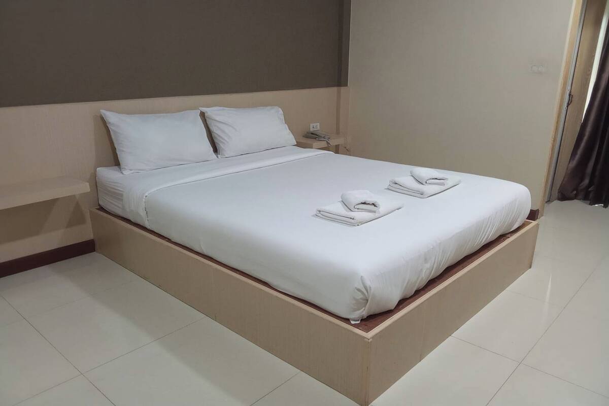 A neatly made bed with white linens and towels, a bedside table with a phone, and a plain wall.