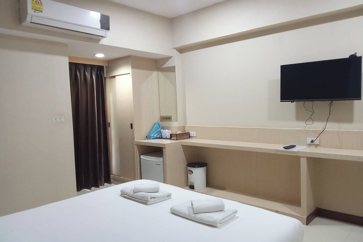 A hotel room with a bed, a TV mounted on the wall, a desk, and a trash bin.