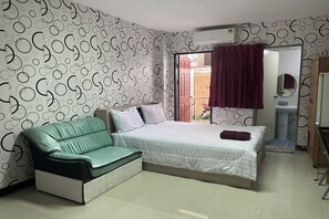 A bedroom with a bed, a green sofa, a wardrobe, and a bathroom visible through an open door. - Green Place 107 (Bangkok)