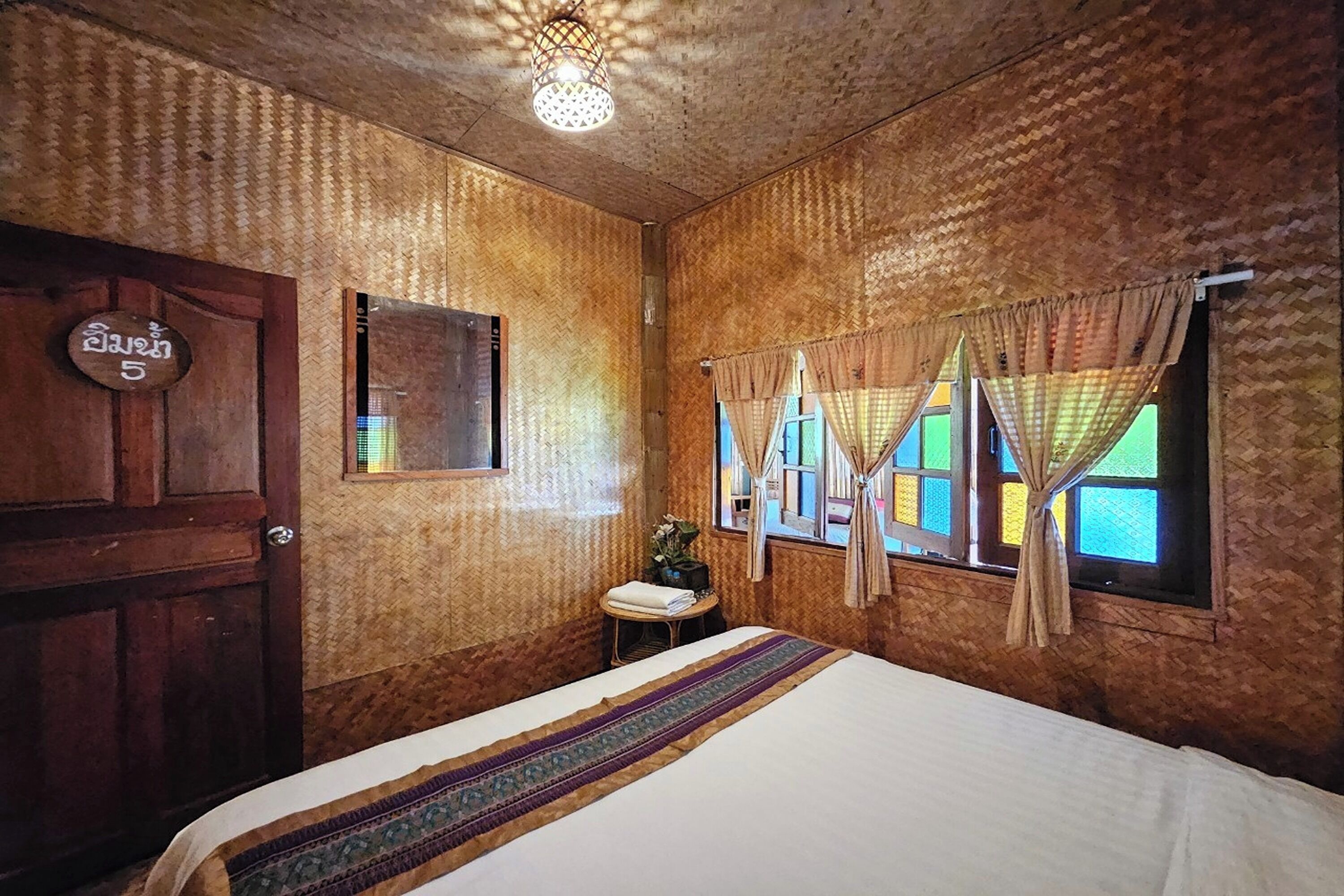 Una habitación con una cama, una puerta de madera, una pequeña mesa con una planta y una ventana con cortinas.